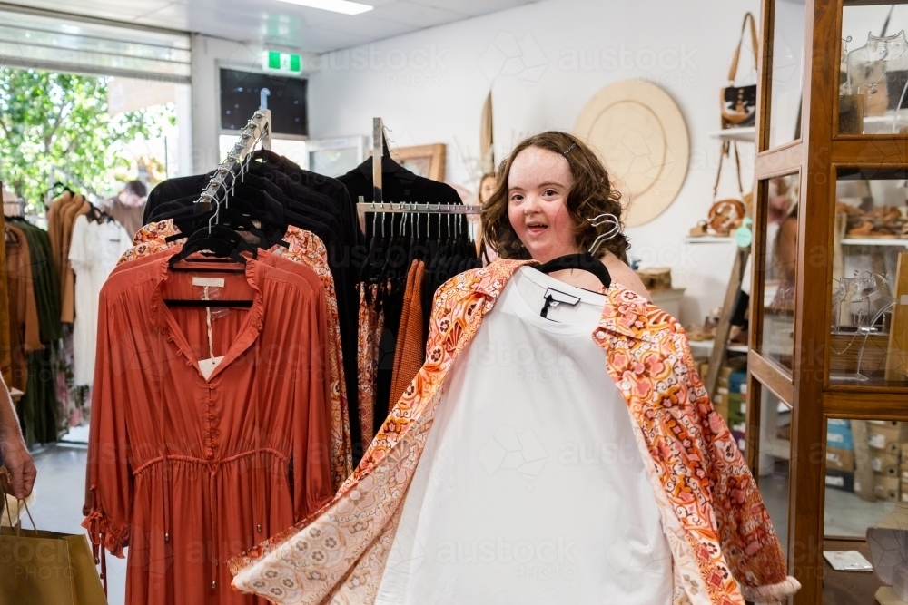Happy young lady with down syndrome shopping in dress and clothing store boutique - Australian Stock Image