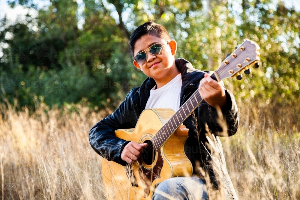 Happy young man playing guitar in grassy bushland - Australian Stock Image