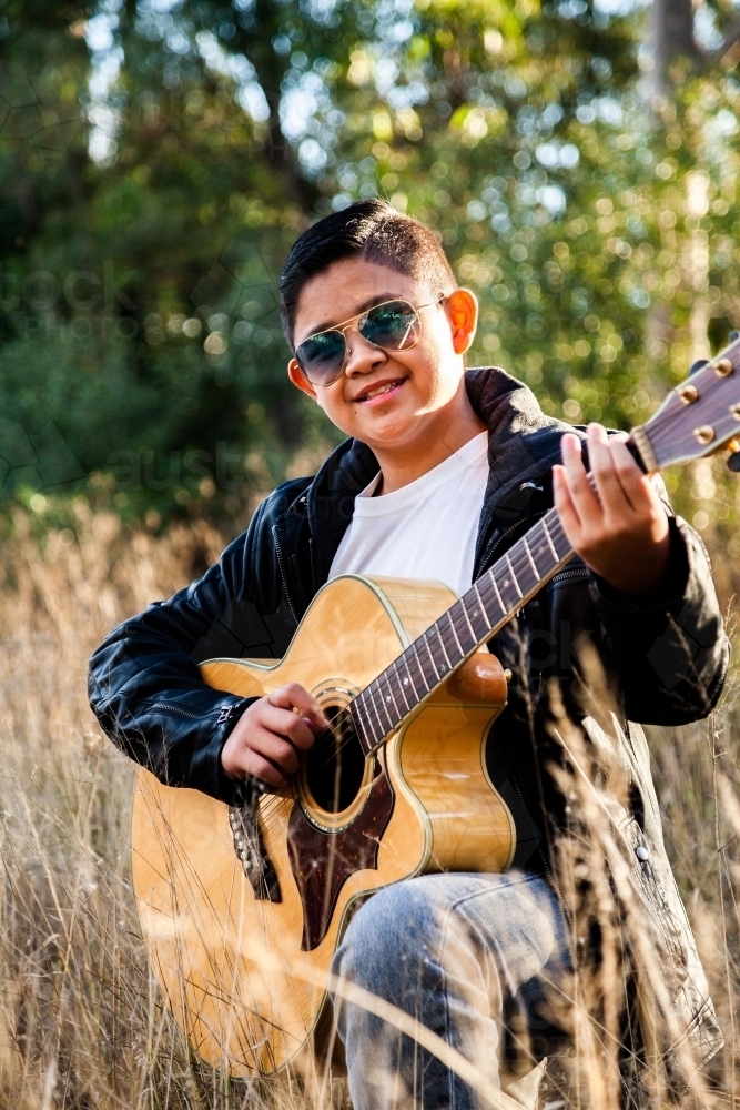 Happy young man playing guitar in grassy bushland - Australian Stock Image