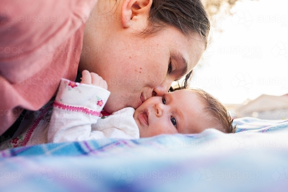 happy young mother playing with her new baby outside on picnic rug - Australian Stock Image