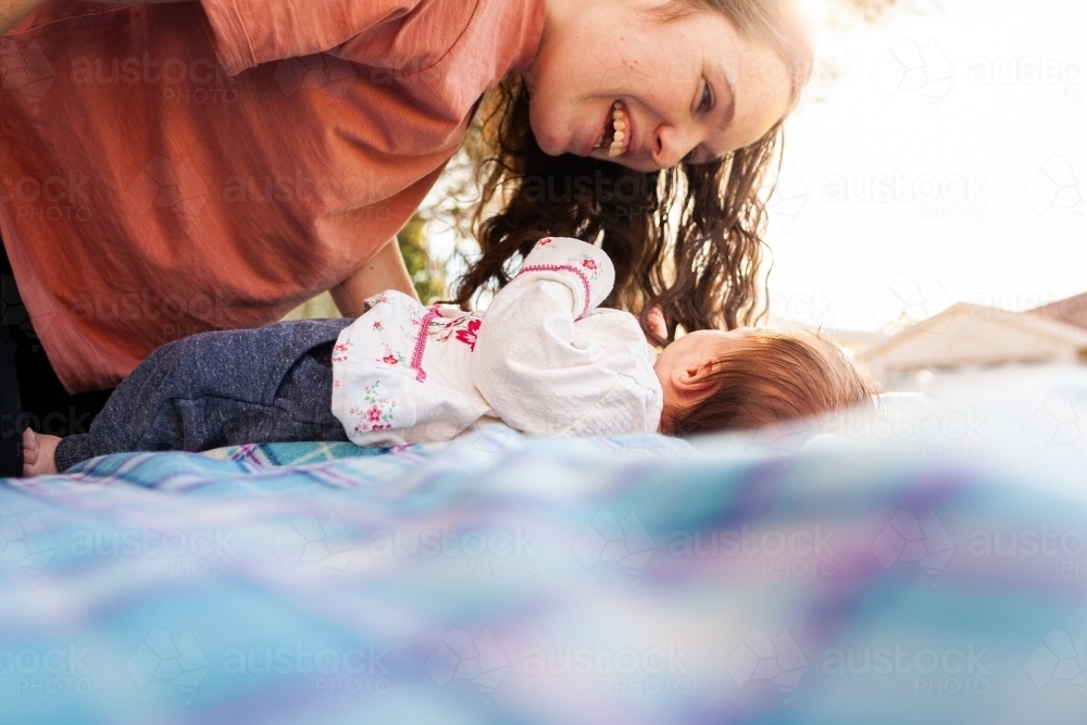 happy young mother playing with her new baby outside on picnic rug - Australian Stock Image