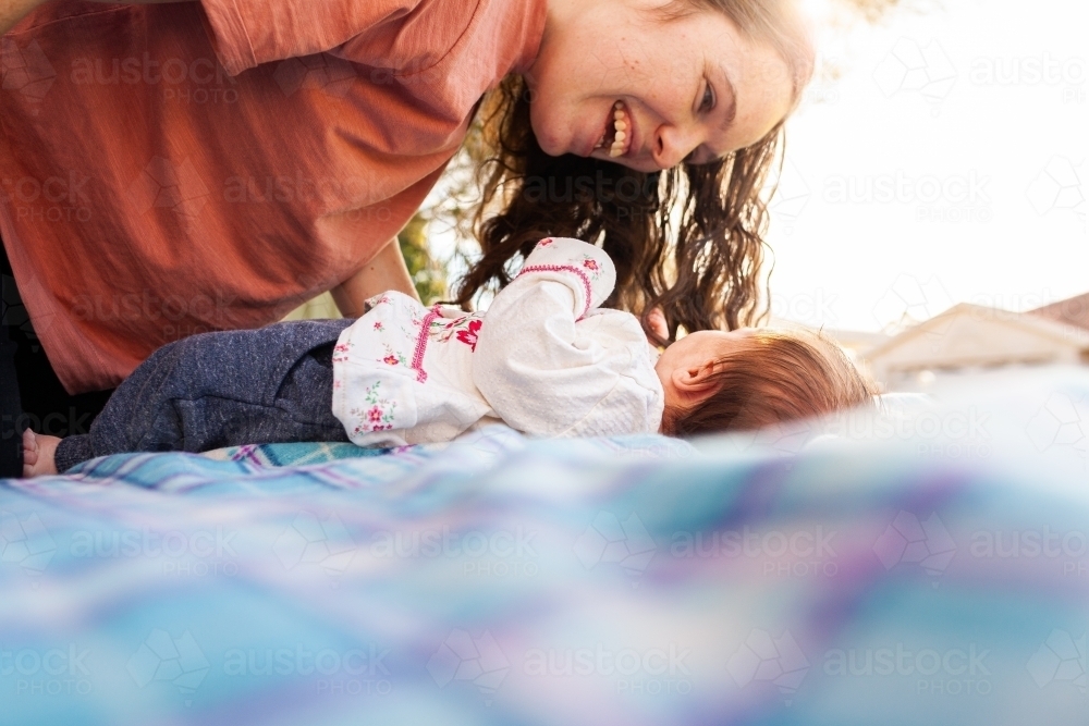 happy young mother playing with her new baby outside on picnic rug - Australian Stock Image