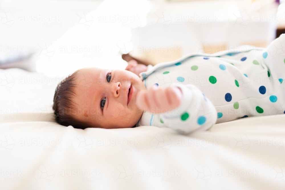 Happy young newborn baby lying on parents bed in bedroom - morning time - Australian Stock Image