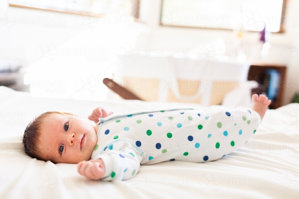 Happy young newborn baby lying on parents bed in bedroom - morning time - Australian Stock Image