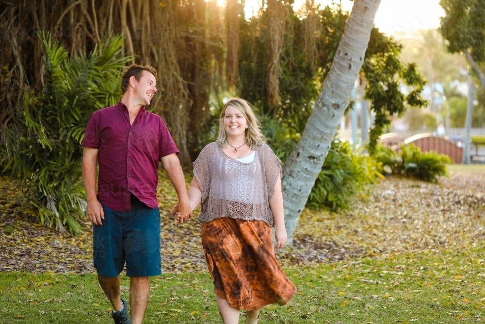 Happy young romantic couple walking together in golden afternoon light at the park - Australian Stock Image
