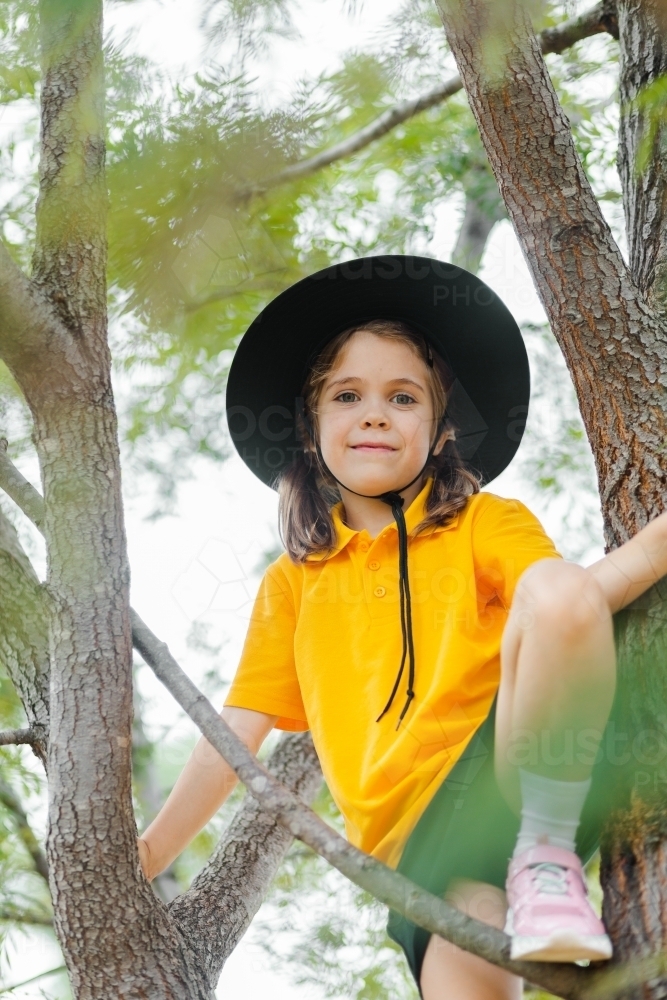 Happy young school girl climbing up tree - Australian Stock Image