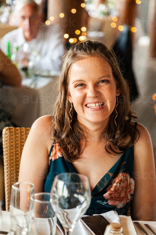 Happy young wedding guest smiling at table during reception - Australian Stock Image