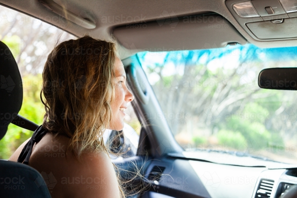 Happy young woman in passenger seat of car coming home from a beach day with friends - Australian Stock Image