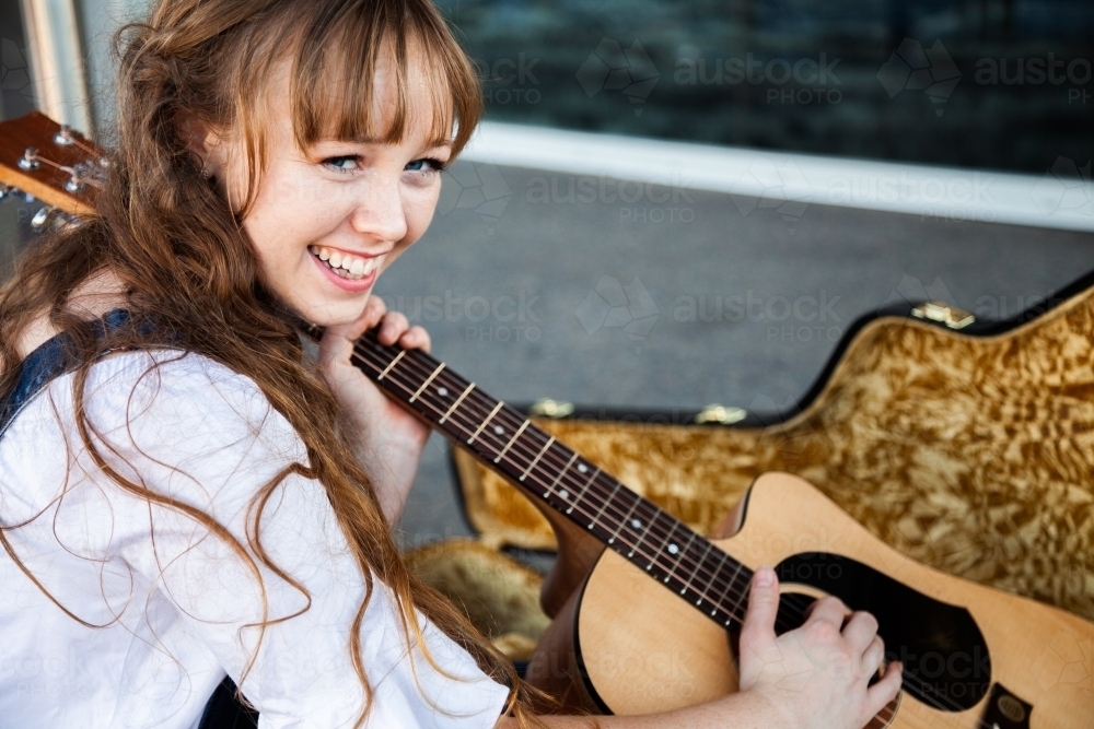 Happy young woman lifting guitar out of case - Australian Stock Image