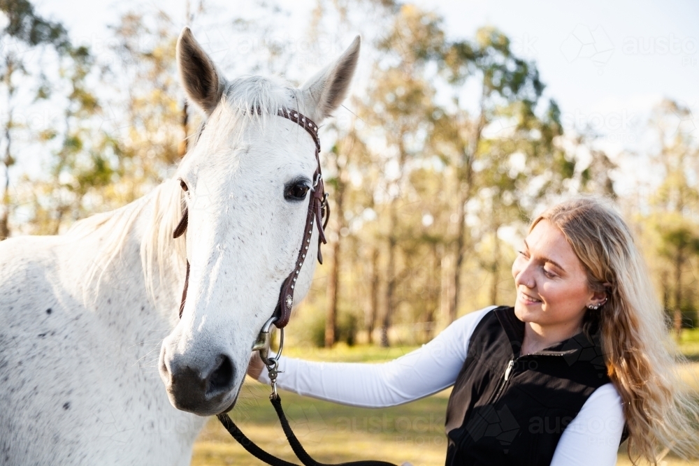 Happy young woman looking at her horse backlit in paddock - Australian Stock Image