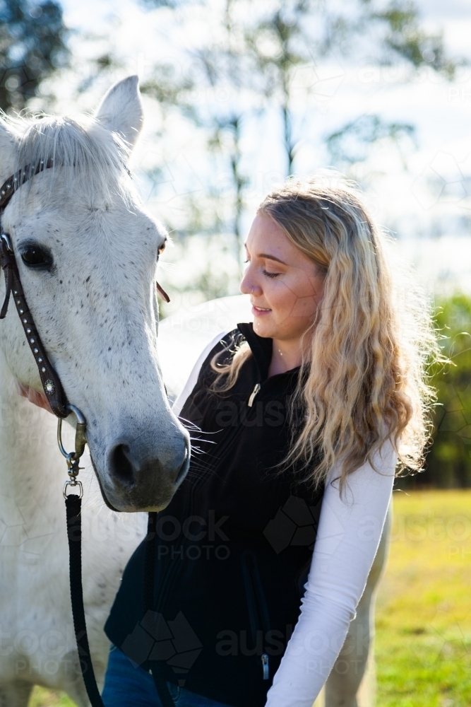 Happy young woman looking at her horse backlit in paddock - Australian Stock Image