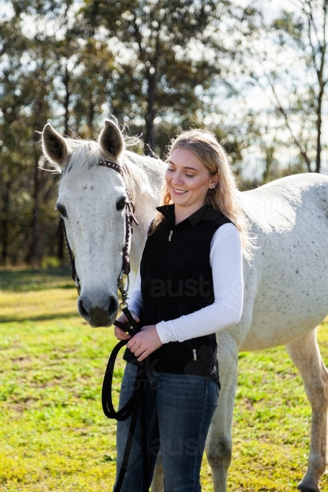 Happy young woman looking at her horse backlit in paddock - Australian Stock Image