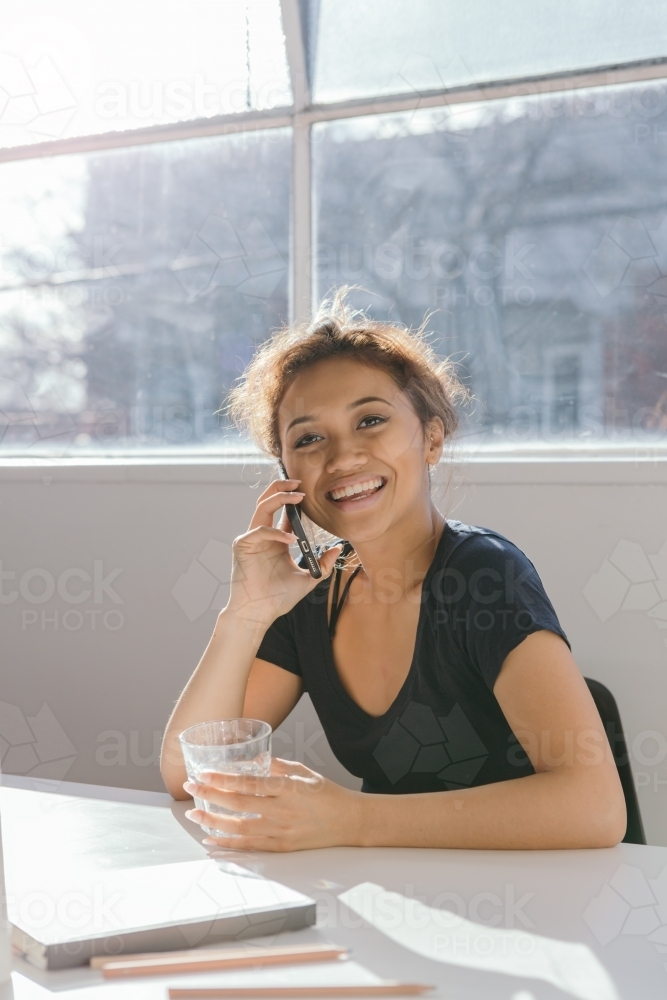 Happy young woman on the phone holding a glass - Australian Stock Image