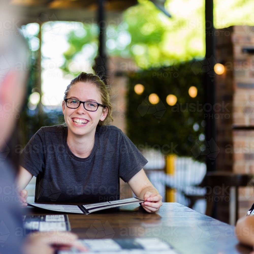 Happy young woman ordering food from menu at cafe - Australian Stock Image