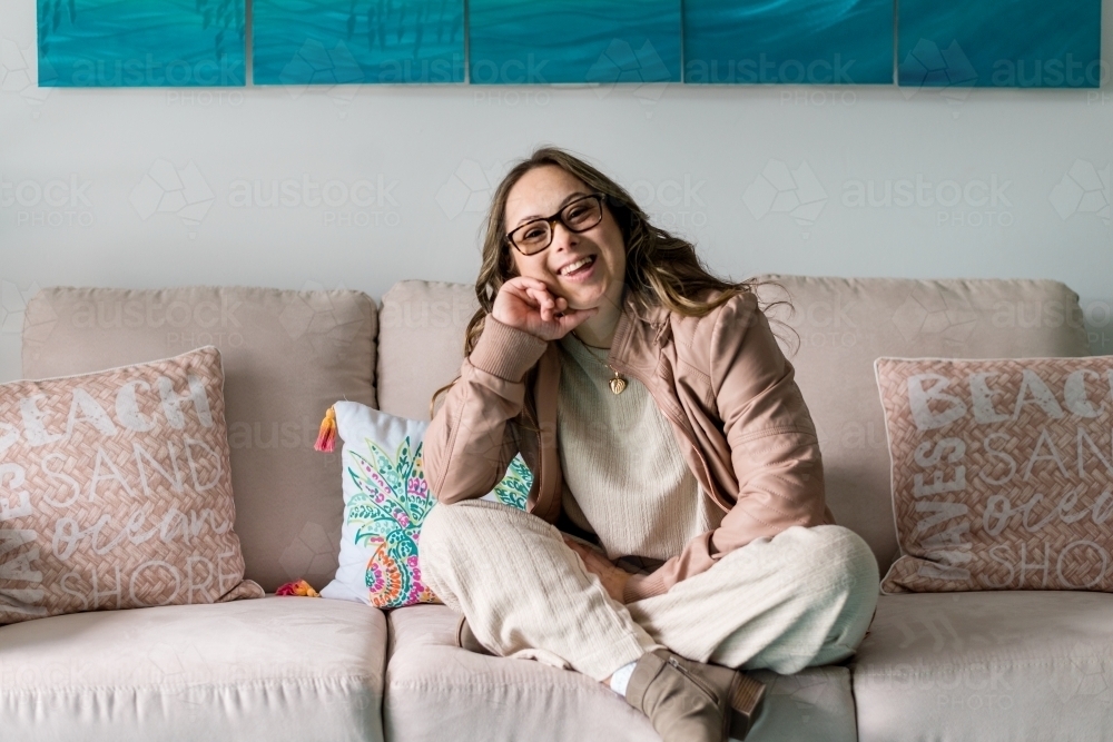 happy young woman with down syndrome, sitting on couch - Australian Stock Image