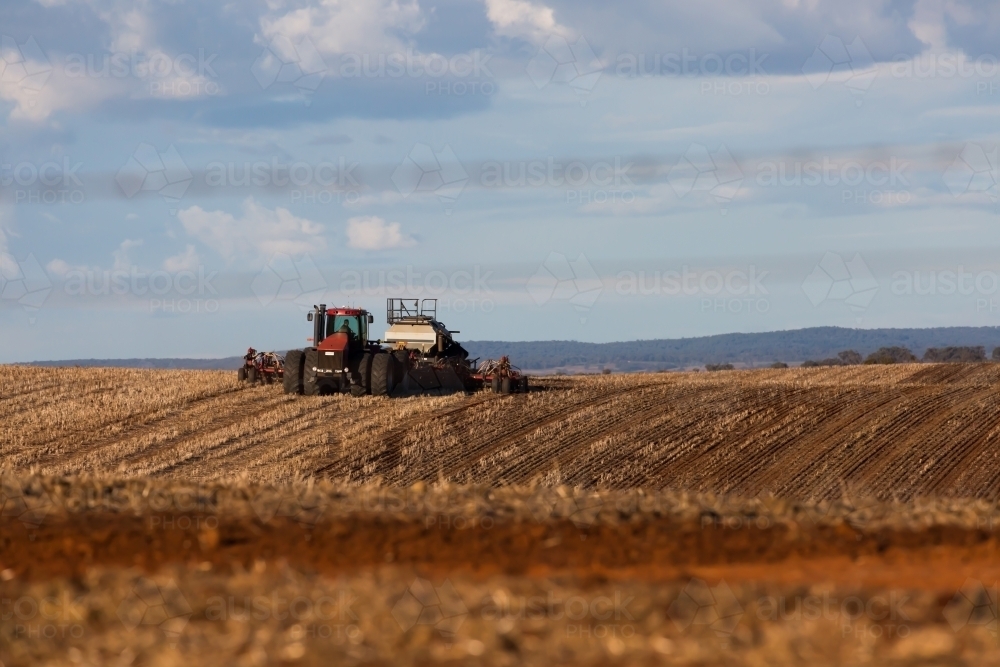 Harvesting tractor ploughing a dry field - Australian Stock Image
