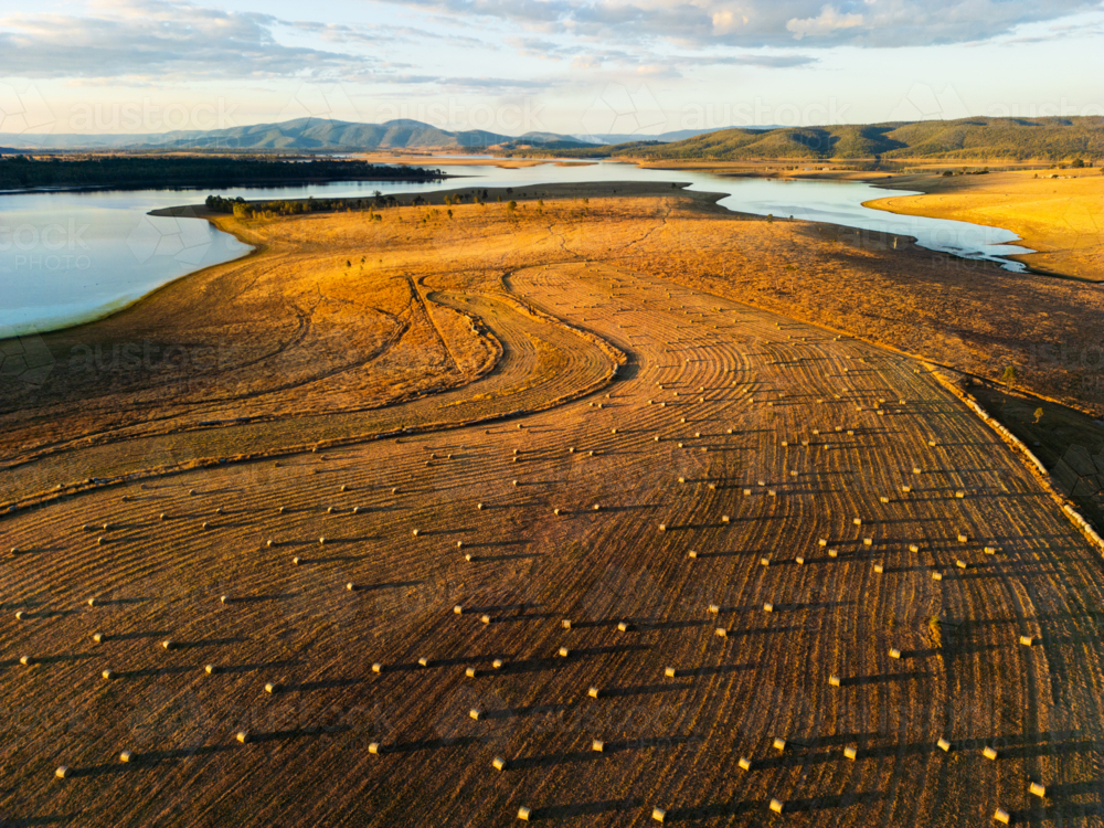 Hay bales dotted in a paddock with Lake Wivenhoe in the background - Australian Stock Image