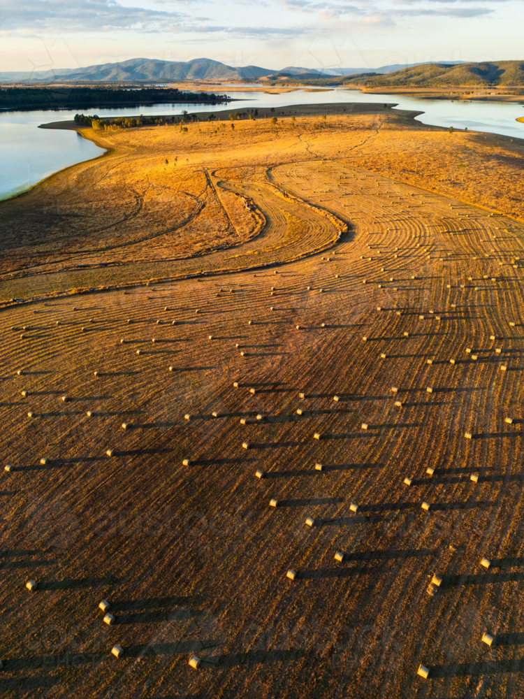 Hay bales dotted in a paddock with Lake Wivenhoe in the background - Australian Stock Image