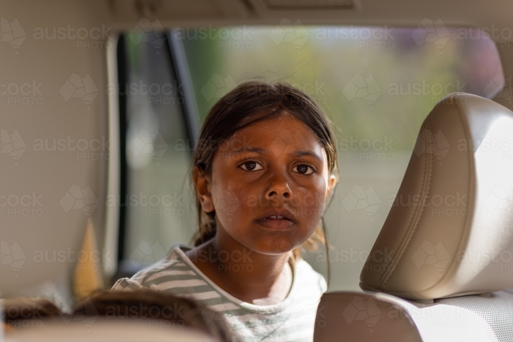 head and shoulders of aboriginal child with dirty face sitting in back seat of a car - Australian Stock Image