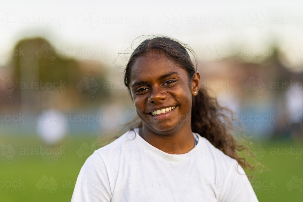head and shoulders of aboriginal girl looking straight on and wearing white t-shirt - Australian Stock Image