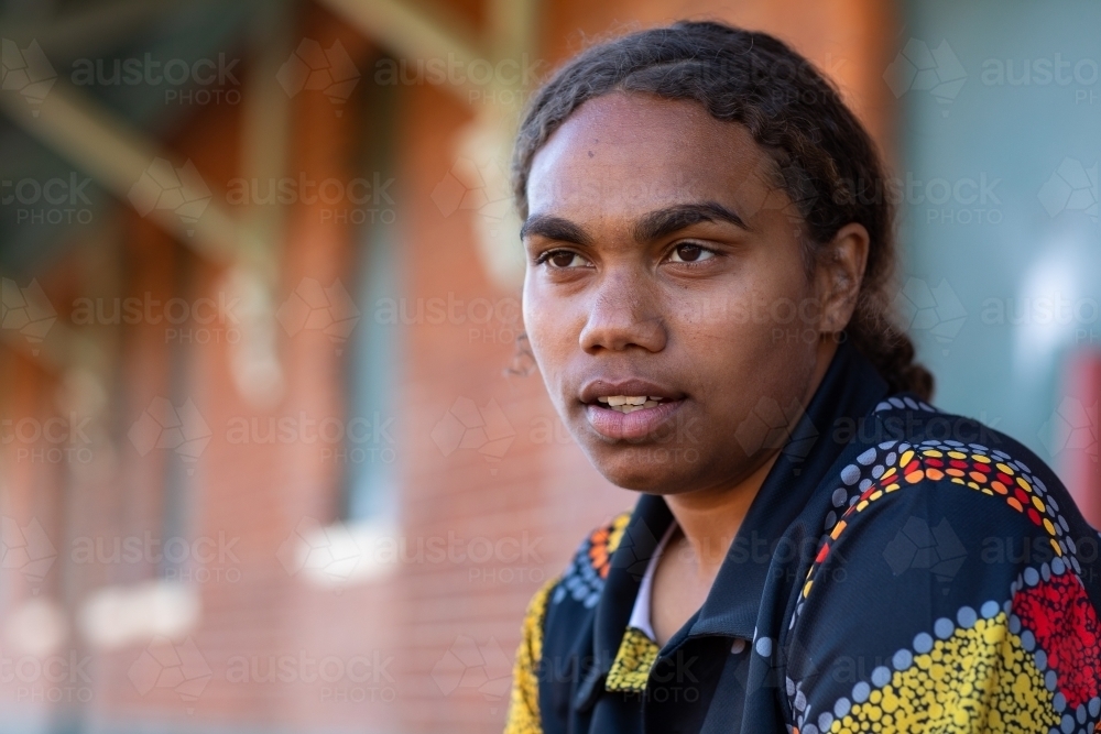 head and shoulders of aboriginal girl with hair tied back in front of brick wall - Australian Stock Image