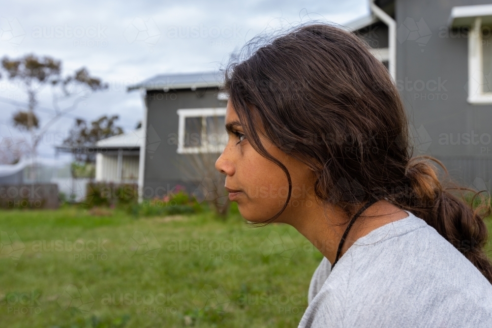 head and shoulders of aboriginal teen girl in profile with house in background - Australian Stock Image