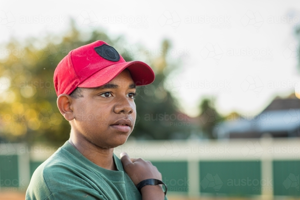head and shoulders of adolescent wearing red baseball cap looking off into distance - Australian Stock Image