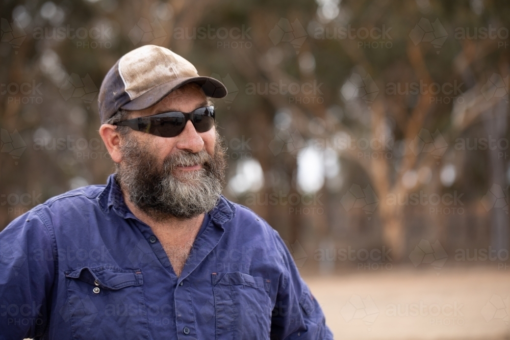 head and shoulders of bearded man wearing sunglasses and cap - Australian Stock Image