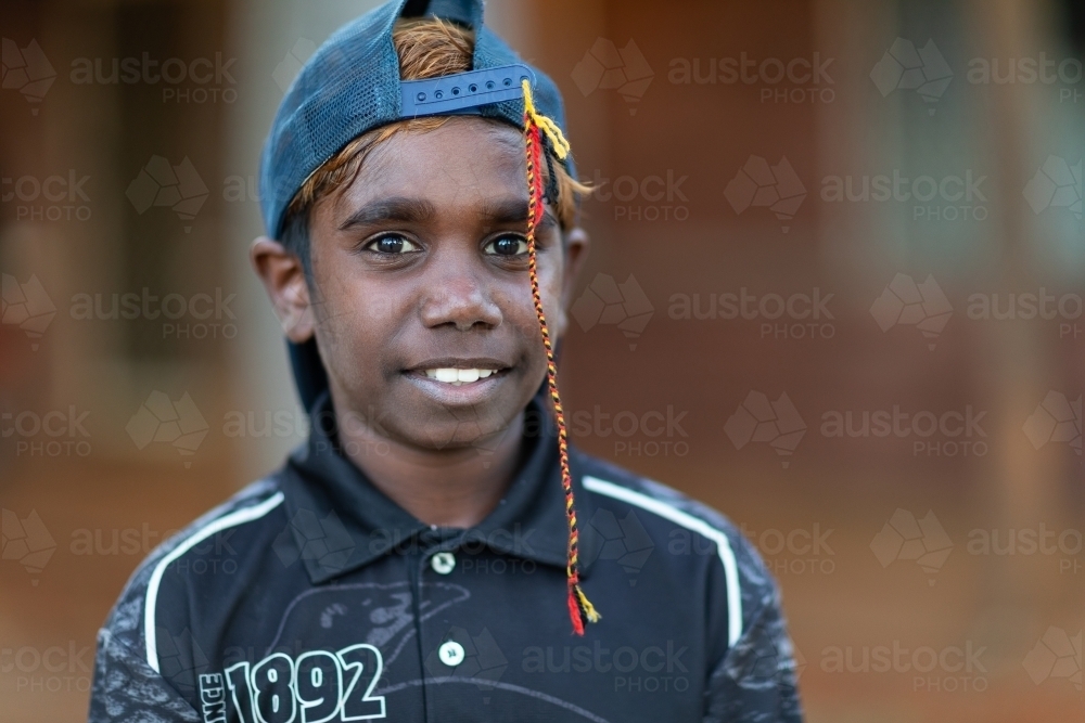 head and shoulders of child with cap on backwards and plaited string hanging down over face - Australian Stock Image