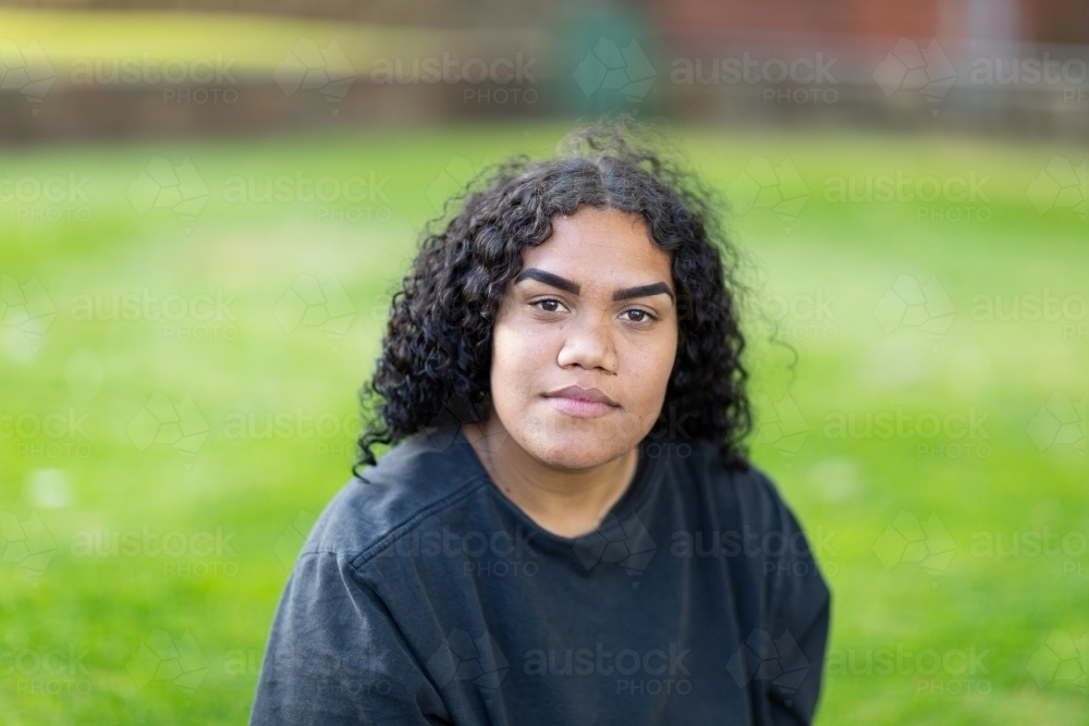 head and shoulders of confident teenage girl with curly hair wearing dark jumper looking at camera - Australian Stock Image