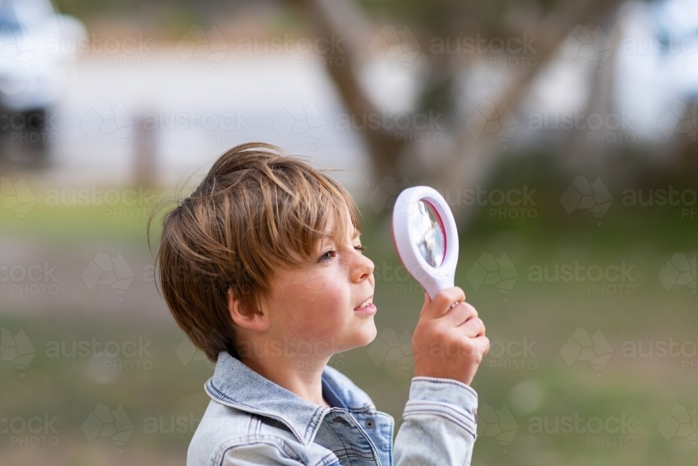 head and shoulders of curious child looking through magnifying glass - Australian Stock Image