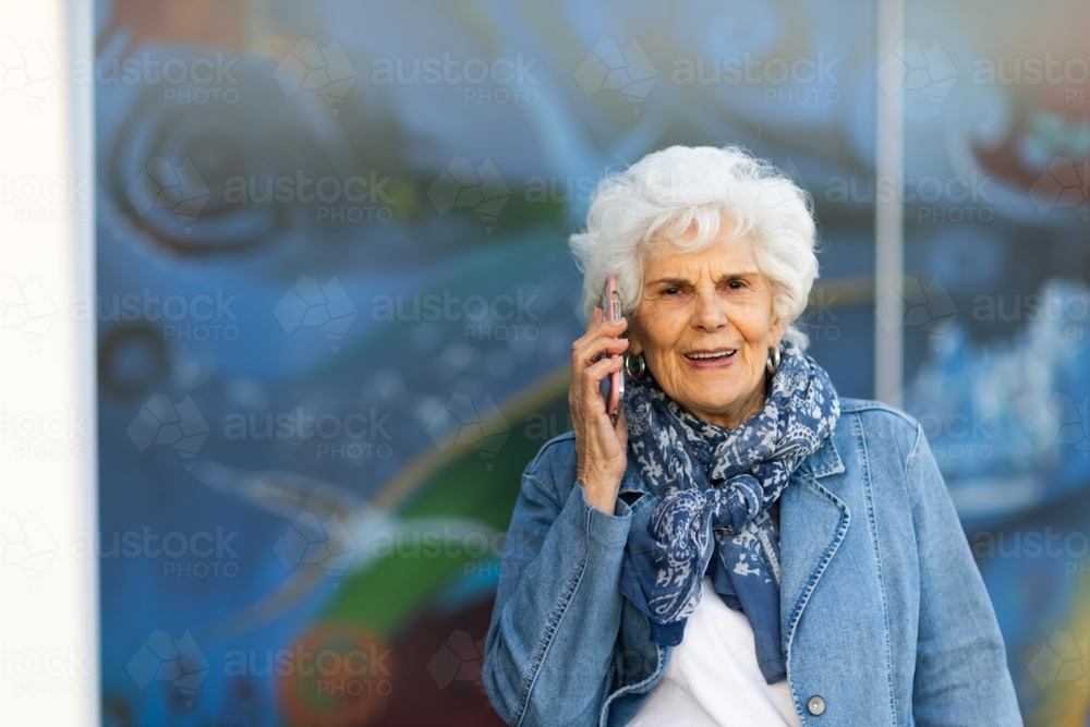 head and shoulders of elderly woman with white hair holding phone to her ear - Australian Stock Image