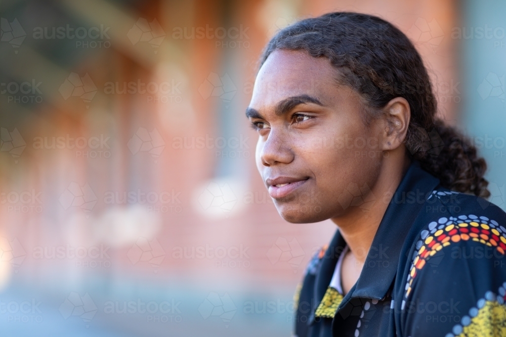 head and shoulders of indigenous girl with hair tied back and blurry building in background - Australian Stock Image