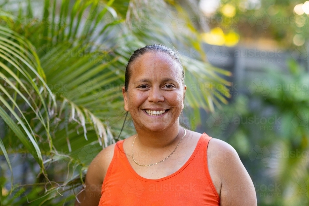 head and shoulders of indigenous woman in front of tropical greenery - Australian Stock Image