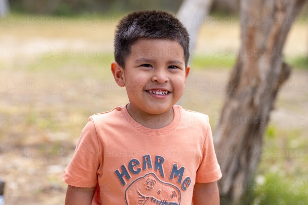 head and shoulders of little boy with black hair smiling and squinting - Australian Stock Image