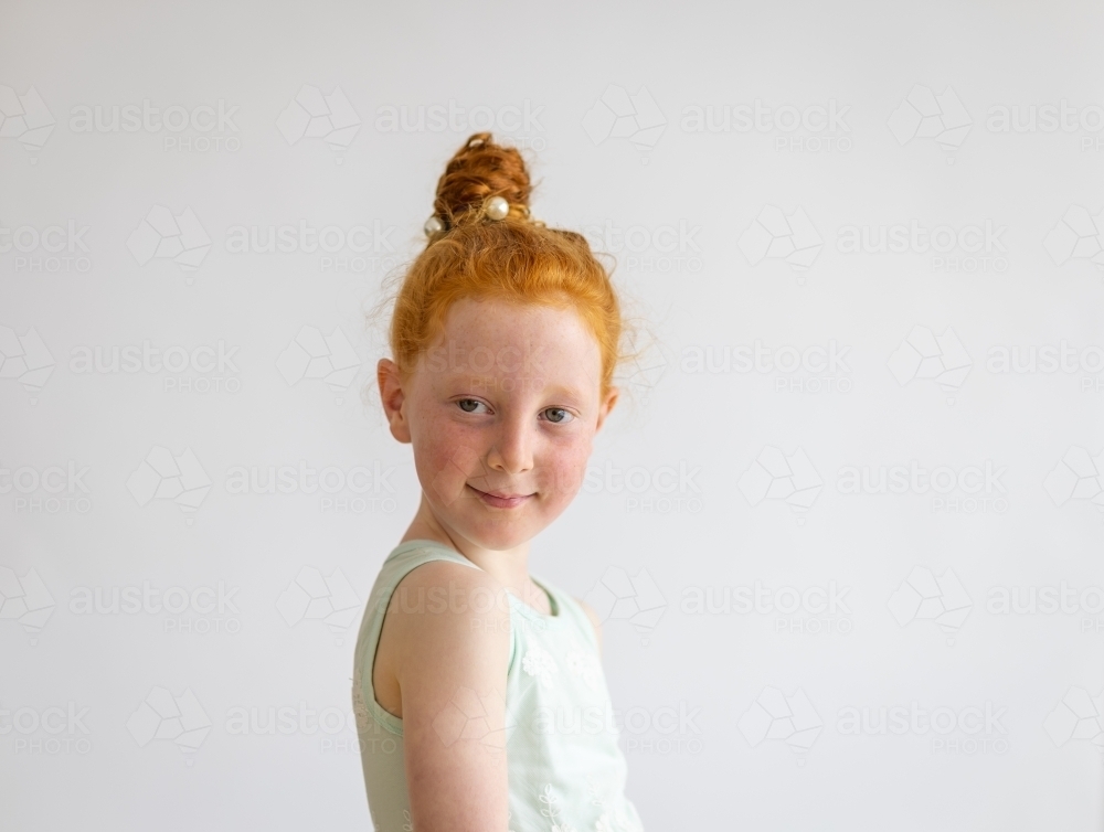 head and shoulders of little girl looking over her shoulder on plain white background - Australian Stock Image