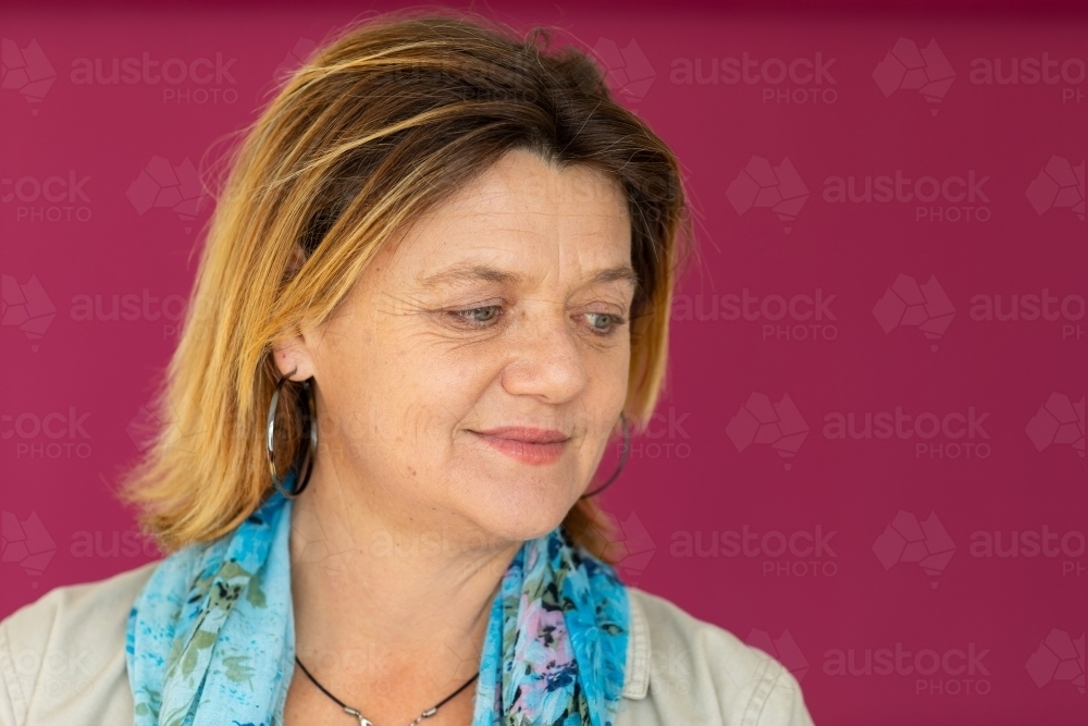head and shoulders of mature woman against dark pink background - Australian Stock Image