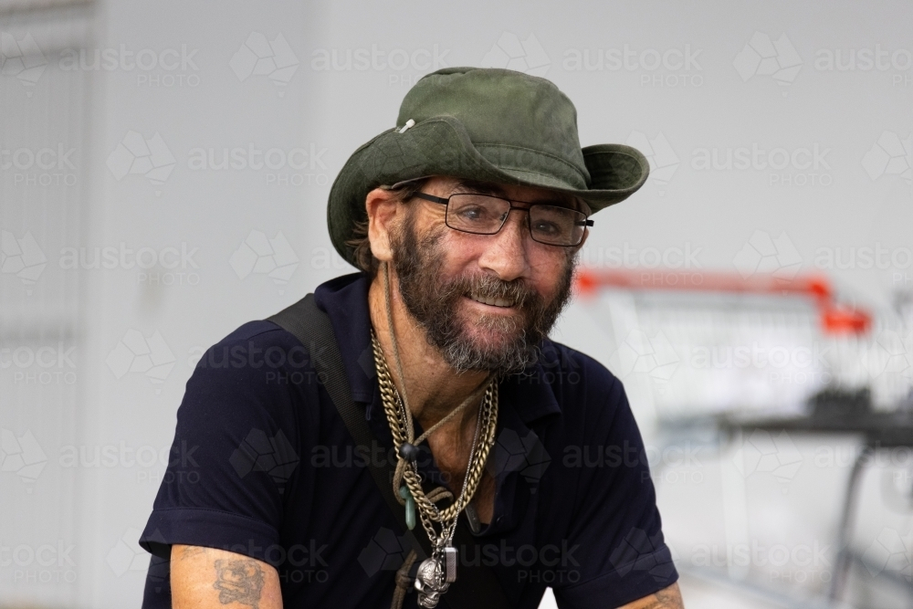head and shoulders of scruffy man wearing hat and black tee shirt - Australian Stock Image