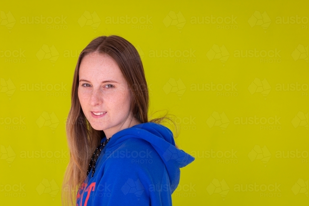 head and shoulders of teenage girl in blue hoody against green background - Australian Stock Image