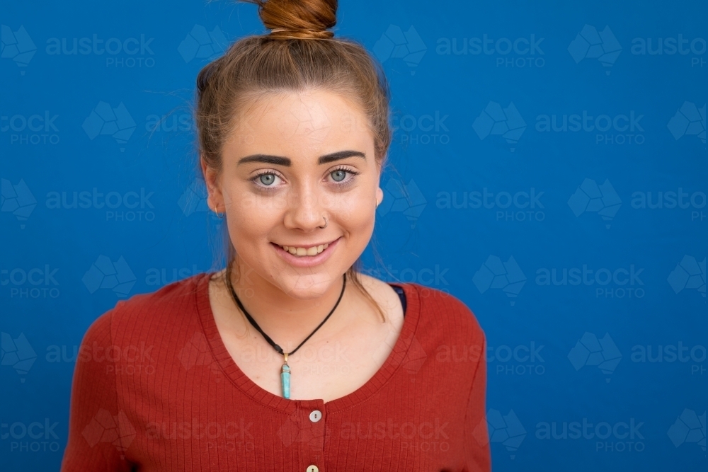 head and shoulders of teenage girl smiling at camera on blue background - Australian Stock Image