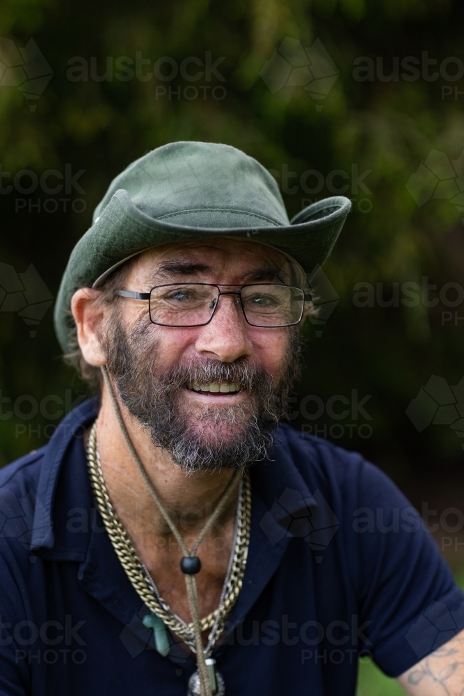 head and shoulders of unkempt man smiling and wearing a hat - Australian Stock Image