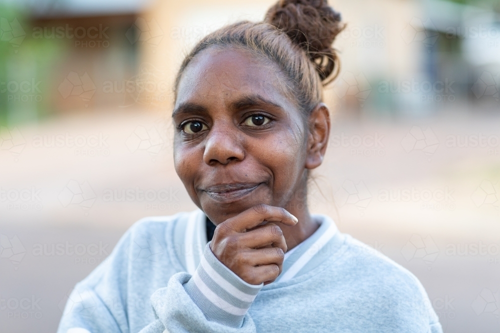 head and shoulders of young aboriginal woman looking at camera with hand to chin - Australian Stock Image
