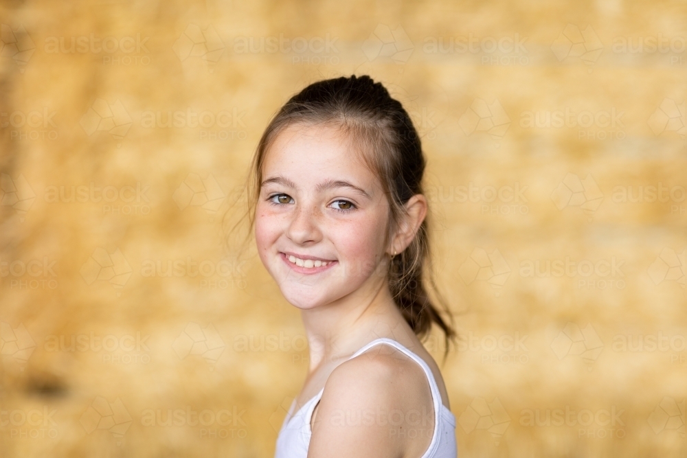 head and shoulders of young caucasian girl with hair tied back wearing white singlet - Australian Stock Image