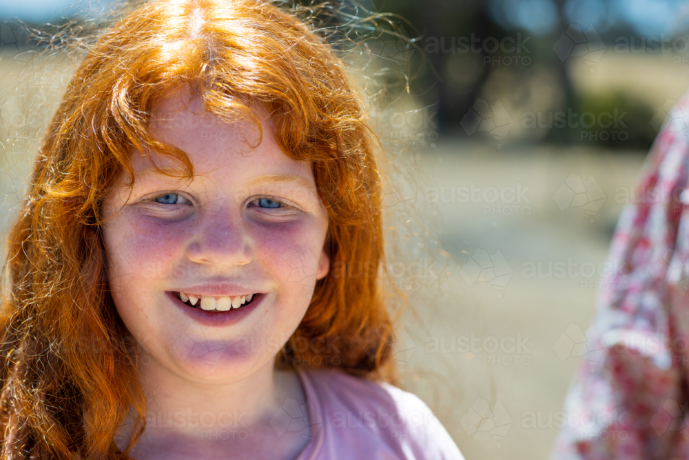 head and shoulders of young fair-skinned girl with orange hair smiling - Australian Stock Image