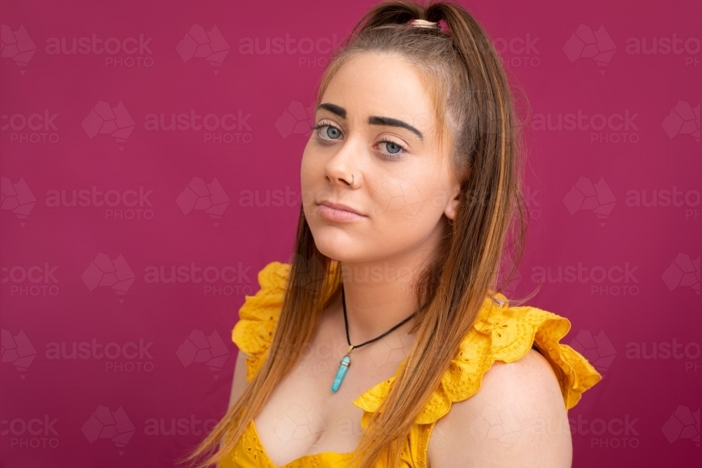head and shoulders of young teen girl looking at camera against pink background - Australian Stock Image