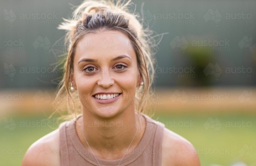 head and shoulders of young woman with hair in messy bun looking at camera - Australian Stock Image