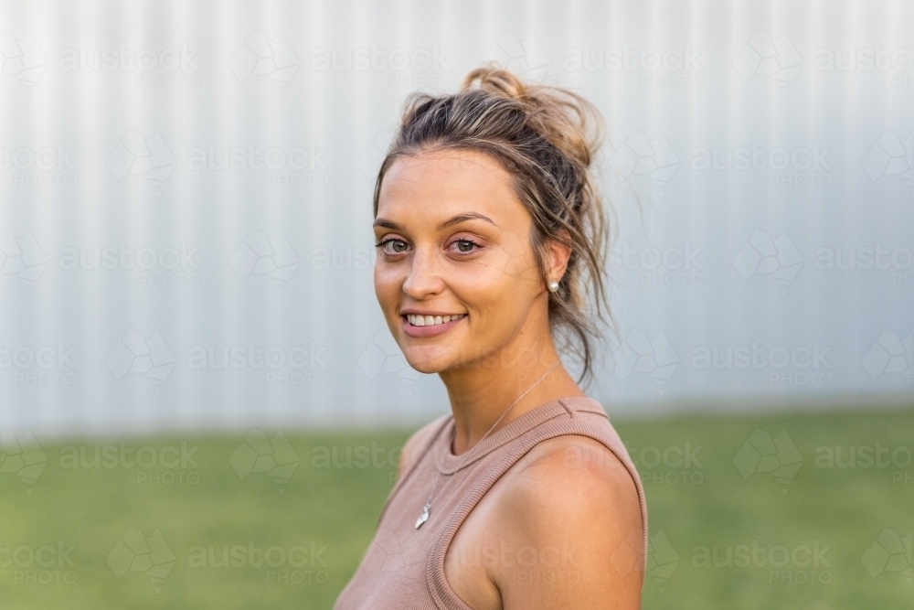 head and shoulders of young woman with hair in messy bun outside - Australian Stock Image