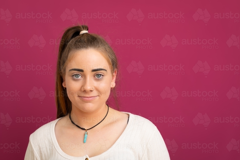 head and shoulders of young woman with high pony tail on pink background - Australian Stock Image