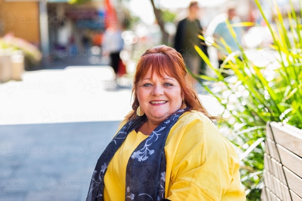 Headshot of happy smiling middle age woman wearing yellow in urban setting - Australian Stock Image