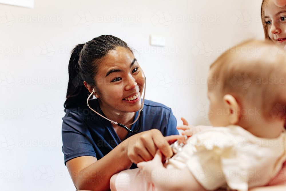 Healthcare worker listens to a baby's chest with a stethoscope while being held by mum - Australian Stock Image